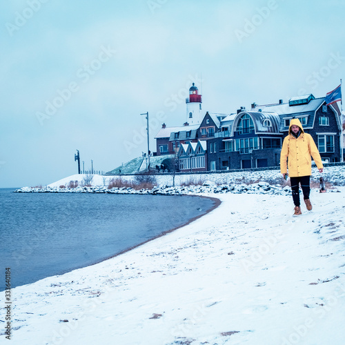 young men in yellow rain jacket walking on a snowy beach by the lighthouse of Urk Netherlands, men with oil lamp and ranin coat photo