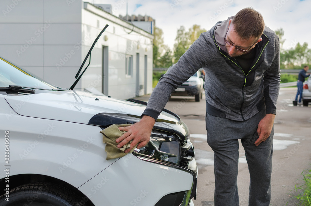 The headlight on the hood of the car is wiped off with water droplets with a microfiber cloth The headlight on the hood of the car is wiped off with water droplets with a microfiber cloth