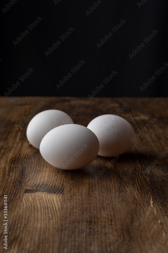 Top view of three white eggs on dark wooden table, with selective focus and black background, in vertical, with copy space