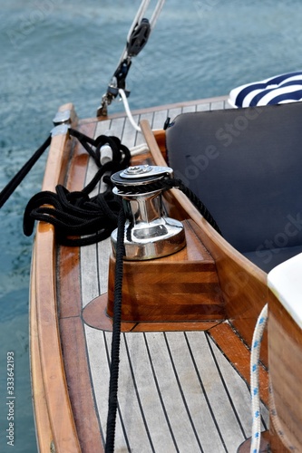 Wooden sailboat moored at the marina. Details of a classic beautiful sailing yacht with teak deck, varnished wood, winch and ropes on blurred background