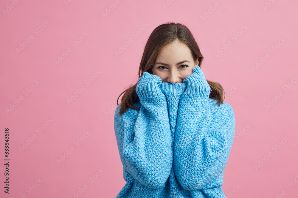 Portrait of happy and lovely young woman in a blue winter sweater on a pink background Portrait of happy and lovely young woman in a blue winter sweater on a pink background