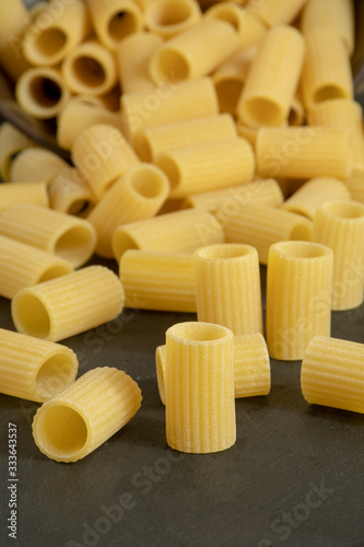 Raw Mezze maniche rigate Italian pasta  on black background, selective focus.
