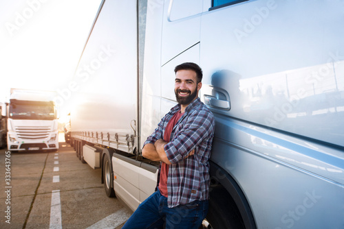 Portrait of young Caucasian bearded trucker with arms crossed standing by his truck vehicle. Transportation service. photo