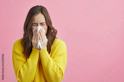 Pretty girl is Sneezing into a tissue because of her allergy or cold  photo