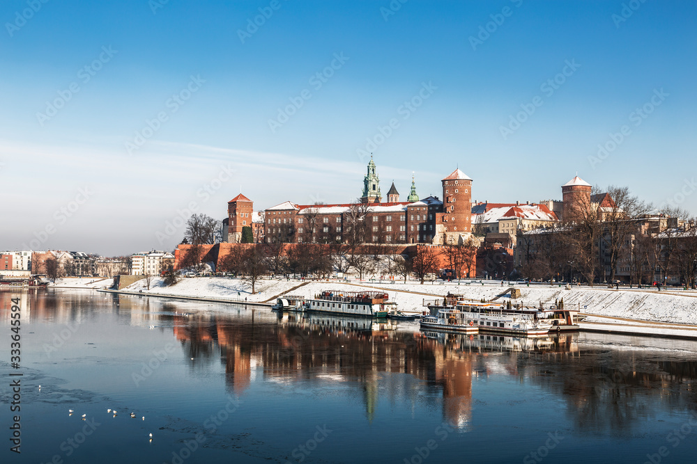 Ancient Royal Wawel castle on the banks of the Vistula river with tourist boats at the pier in winter, Krakow, Poland
