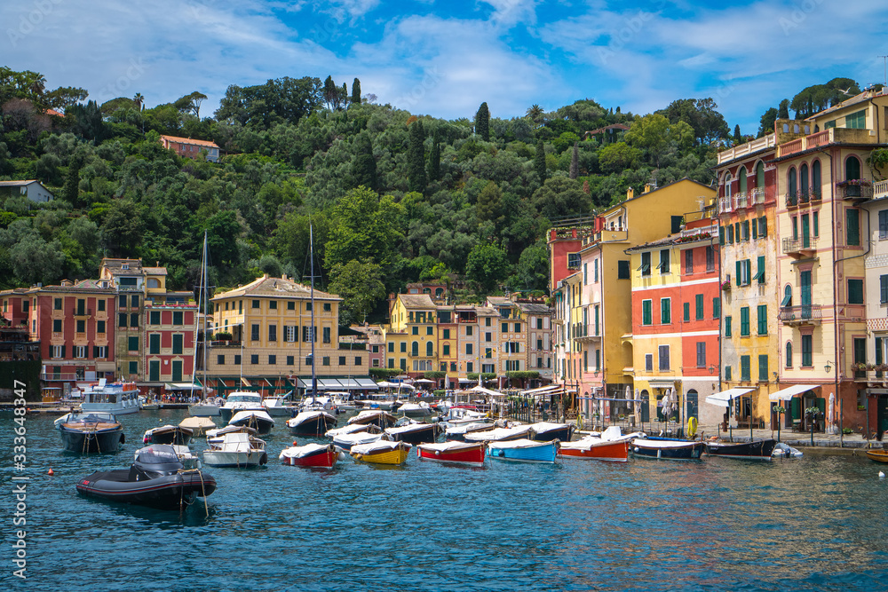 Stunning panoramic view of Portofino, one of the world’s most beautiful seaside towns on the Italian Riviera. Mediterranean landscape of yacht-filled harbor and colorful buildings on a sunny day.