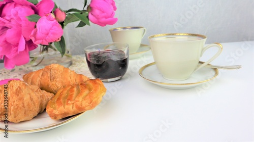 breakfast with two cups of coffee and croissants, bouquet of pink flowers