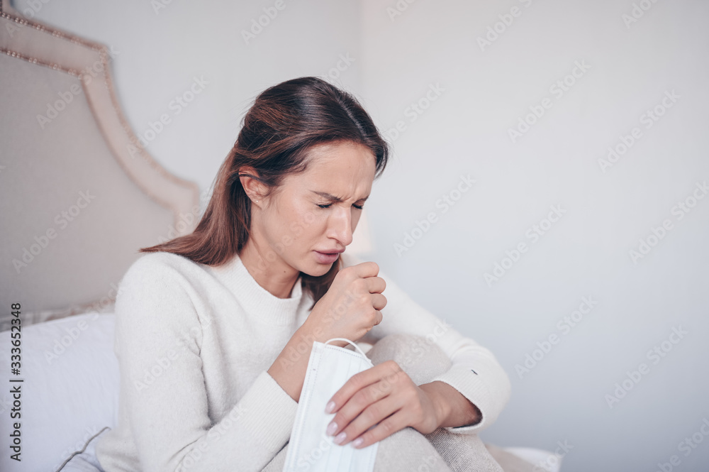 Coronavirus disease (COVID-19) symptoms - runny nose, sore throat, cough, fever. Young woman with face mask sick of flu viral infection spreading corona virus lying in bed at home quarantine isolation Coronavirus disease (COVID-19) symptoms - runny nose, sore throat, cough, fever. Young woman with face mask sick of flu viral infection spreading corona virus lying in bed at home quarantine isolation