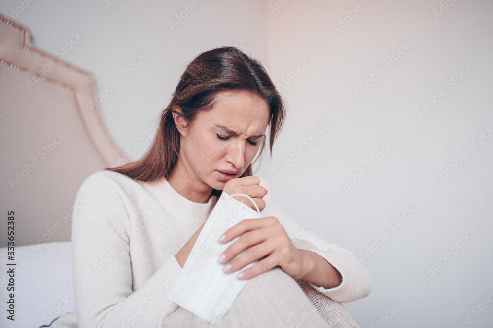 Coronavirus disease (COVID-19) symptoms - runny nose, sore throat, cough, fever. Young woman with face mask sick of flu viral infection spreading corona virus lying in bed at home quarantine isolation Coronavirus disease (COVID-19) symptoms - runny nose, sore throat, cough, fever. Young woman with face mask sick of flu viral infection spreading corona virus lying in bed at home quarantine isolation