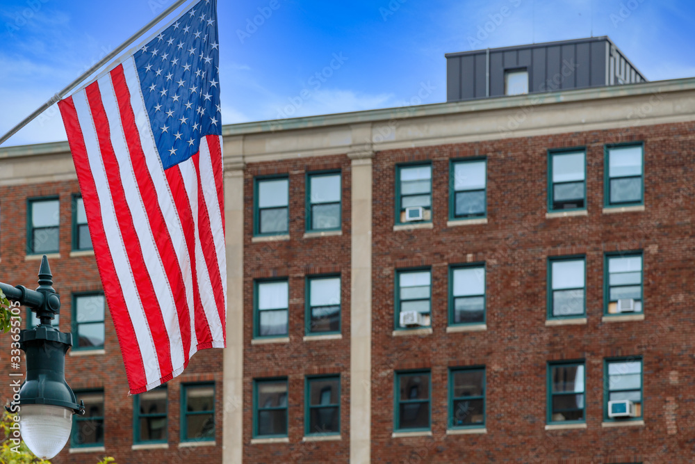 Fototapeta premium An American flag with an old red brick building in the background