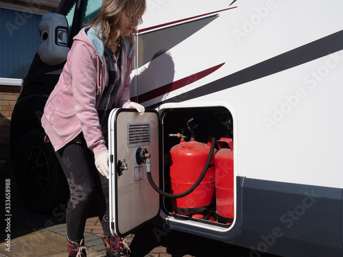 A lady motorhome owner opens a gas locker door wearing gloves.LPG gas bottles can be seen.Image