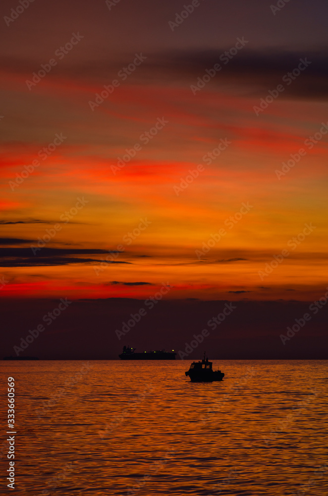 boat anchored over beautiful orange sunset background with cloudy skyline