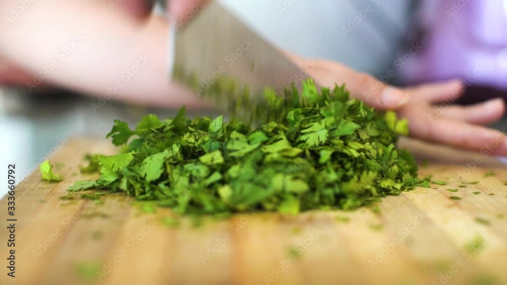 Macro shot oboard of young fair indian woman chopping up dhaniya mint leaves on a wooden chopping board with a huge knife Macro shot oboard of young fair indian woman chopping up dhaniya mint leaves on a wooden chopping board with a huge knife