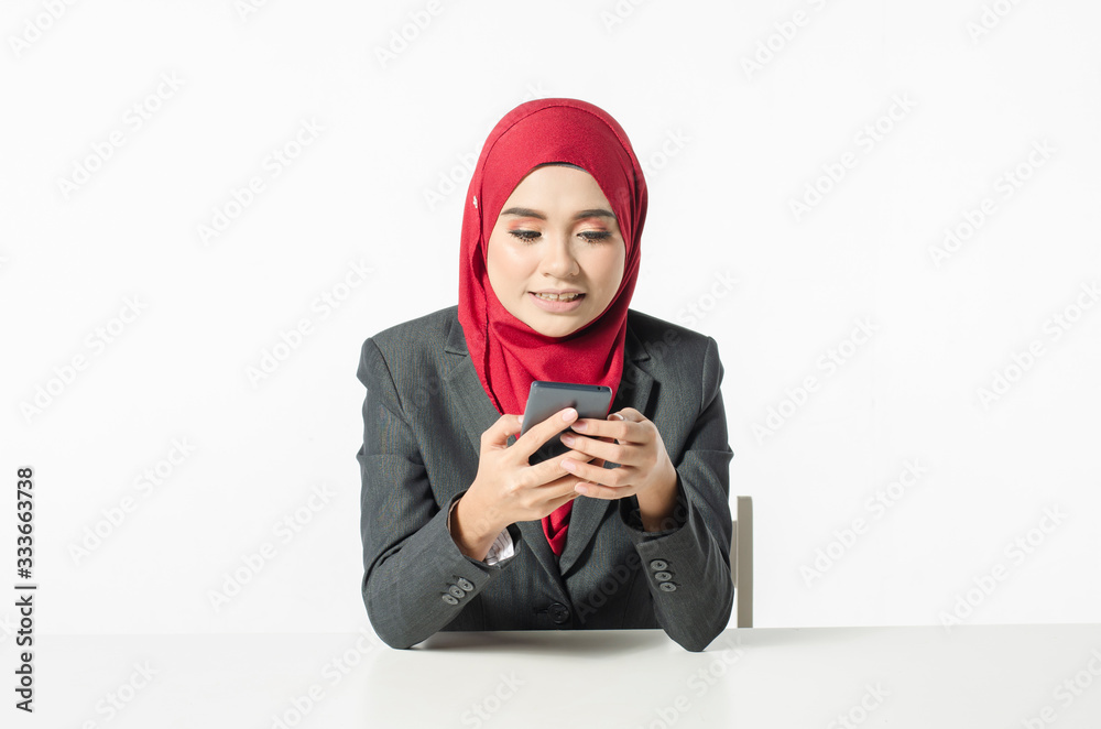 Communication concept, young woman with hijab sitting and texting her friends using her handphone against white background Communication concept, young woman with hijab sitting and texting her friends using her handphone against white background
