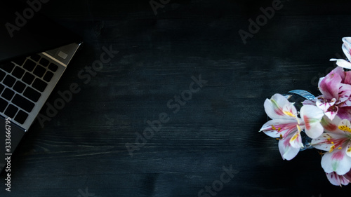 Flat lay home office desk. Working at home women workspace with laptop, flowers bouquet on a dark brown wooden background.