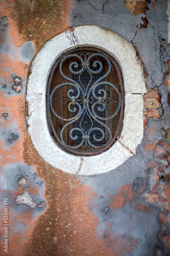 A small beautiful window on an old, historical wall with peeling paint.