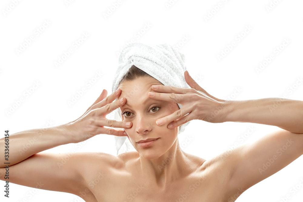 Facial massage at home. Massage the skin around the eyes. Wrinkle smoothing. Beautiful young woman with a white towel on her head and with clean perfect skin. Isolated white background. Facial massage at home. Massage the skin around the eyes. Wrinkle smoothing. Beautiful young woman with a white towel on her head and with clean perfect skin. Isolated white background.
