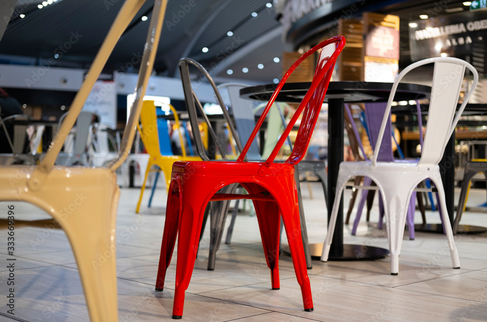 Red metal chair among colored chairs at airport food court.