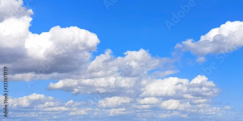 Wide  bright blue sky with large gray-white clouds stretching away into the distance on beautiful sunny day. Tonal perspective. Background  texture or wallpaper in horizontal format