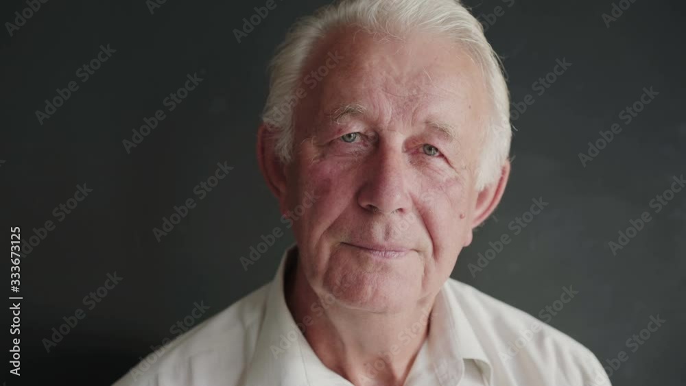Portrait of senior man turns and looks with light smile at camera on background Portrait of senior man turns and looks with light smile at camera on background