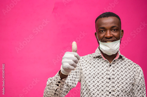 a young african doctor isolated over pink background wearing face mask to prevent himself from the outbreak, disease and flu and did thumbs up.