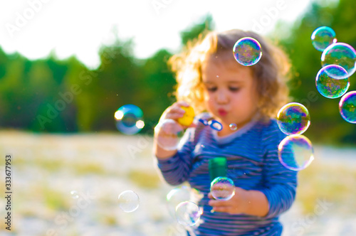 horizontal defocused photo of funny curly-haired girl with soap bubbles