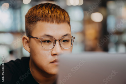 Asian young man indoors in cafe. Lifestyle concept photo with copy space. Picture with handsome guy who using protective face mask. Portrait with gray laptop