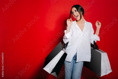 Excited woman with lots of shopping bags dancing isolated on a red background.