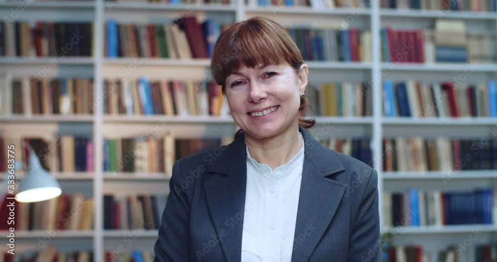 Close-up portrait of professional businesswoman smiling and looking at camera in library next to book rack. Close-up portrait of professional businesswoman smiling and looking at camera in library next to book rack.