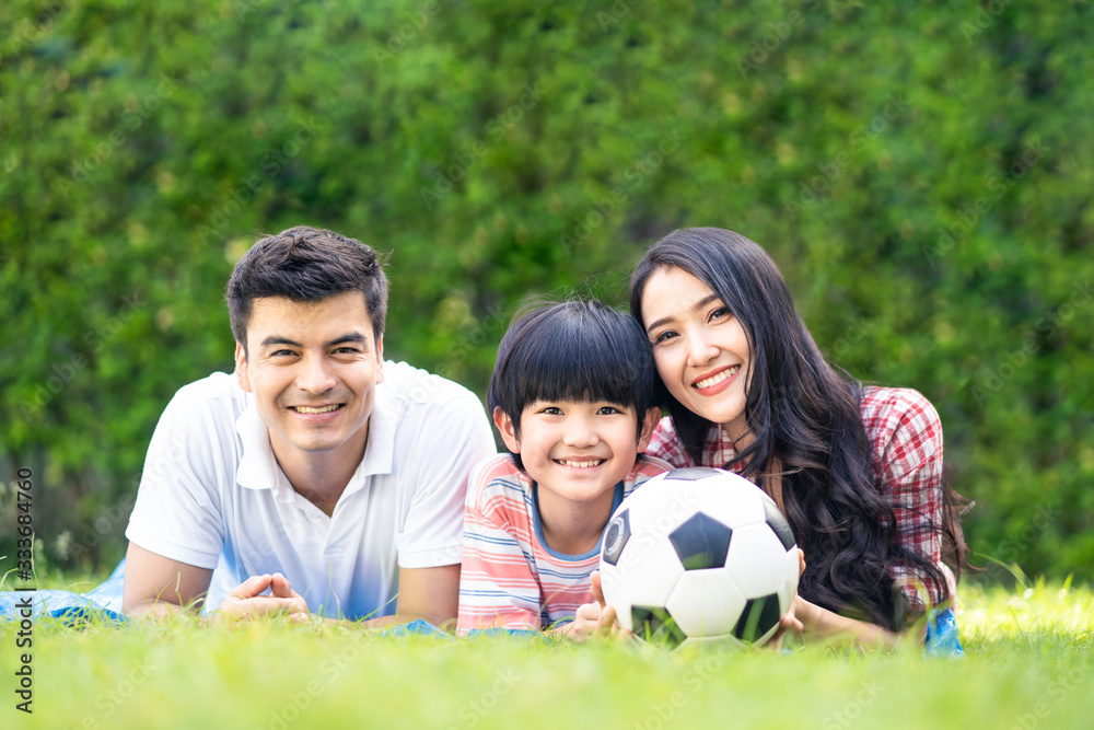 Asian lovely young family are in garden. They lay down on grass and smile with happiness moment. Mother and son hold ball. They love to have leisure and be together. Outdoor lifestyle family concept. Asian lovely young family are in garden. They lay down on grass and smile with happiness moment. Mother and son hold ball. They love to have leisure and be together. Outdoor lifestyle family concept.