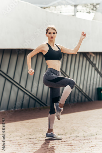 Young woman with fit body jumping and running against grey background. 