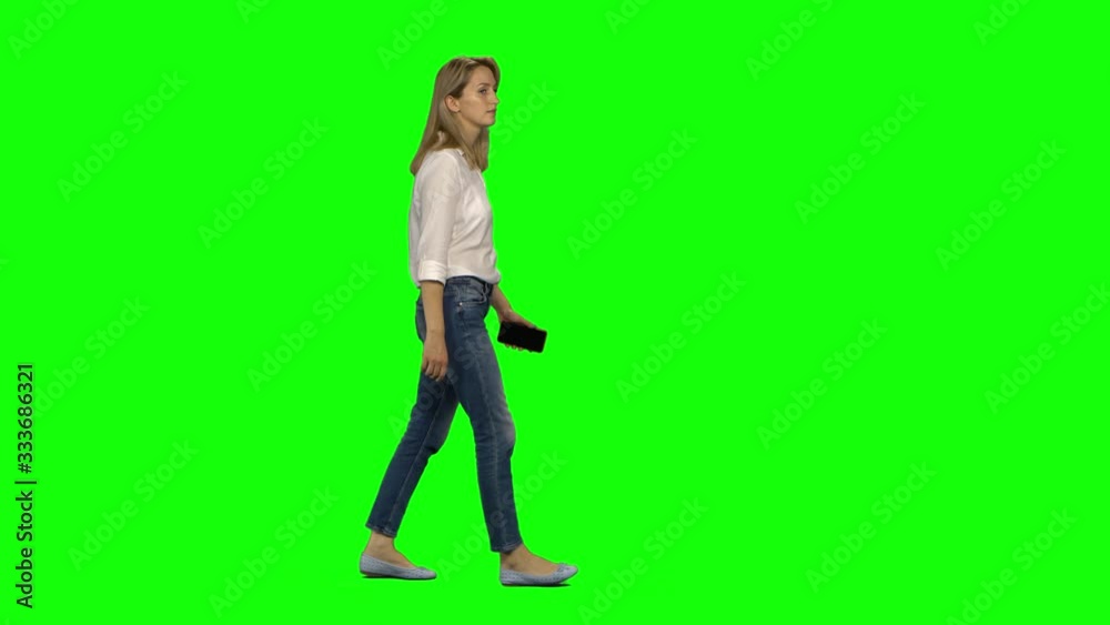 Blonde woman is calmly walking and talking on the mobile phone on green screen. Chroma key, 4k shot. Profile view. Blonde woman is calmly walking and talking on the mobile phone on green screen. Chroma key, 4k shot. Profile view.