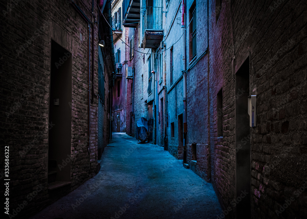 An atmospheric, narrow, back alley painted with blue and magenta light taken in Recanati, Macerata, Italy