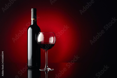 Glass and bottle of red wine on a black reflective background. Copy space.