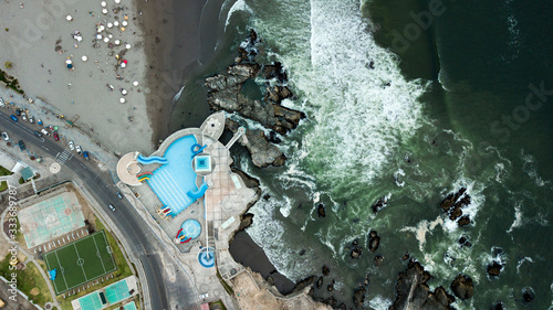 Aerial view on outdoor swimming pool on the coast next to the crushing waves and rocky coast line. Empty swimming pool. Holiday time, families on the beach. Pacific Ocean, Arequipa provincia, Peru  photo