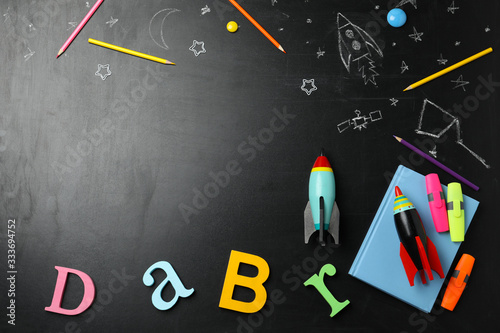 Bright toy rockets, school supplies and drawings on chalkboard, flat lay. Space for text