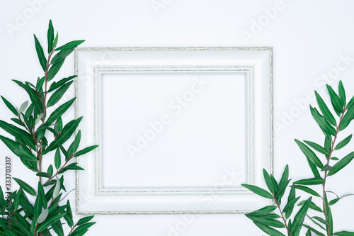 Green leaves with white photo frame on white background. Flat lay  top view  space.