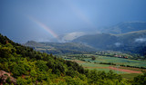 Stunning mountain landscape with lush green rolling hills and double rainbow