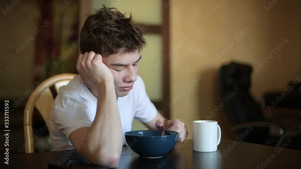 A teenager with a sleepy face idly looks out the window and chews rice porridge, selective focus A teenager with a sleepy face idly looks out the window and chews rice porridge, selective focus