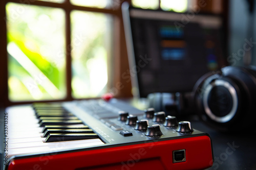 Midi keybard in a music producer home studio, desk with headphones and a notebook. Window with nature in the background.