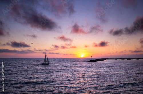 A sailboat in silhouette passes through the sunset over the Pacific Ocean in Redondo Beach, California.