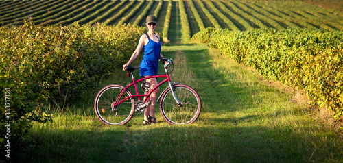 Obraz na płótnie Carefree smiling girl cycling alone in a field among currant bushes in the garden. the best solution to escape from a coronavirus w salonie