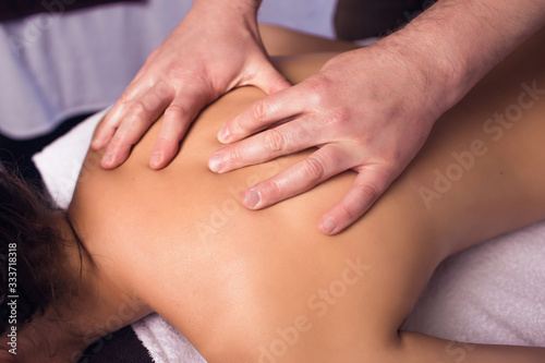 A man gives a massage to a girl in the salon on a massage table in a cozy atmosphere