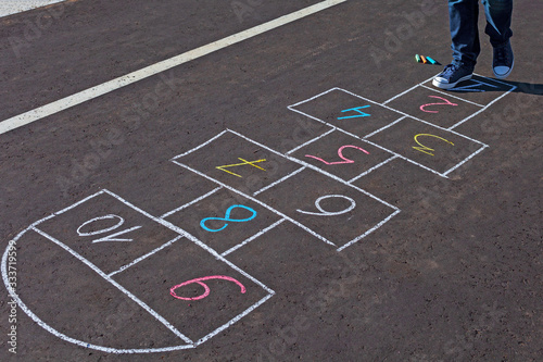 A young man playing hopscotch on asphalt.