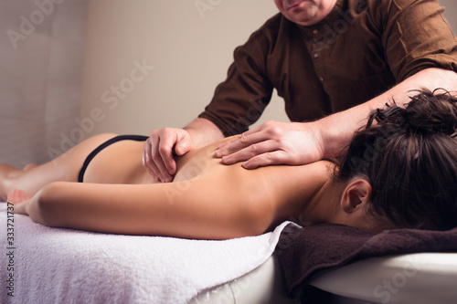 A man gives a massage to a girl in the salon on a massage table in a cozy atmosphere