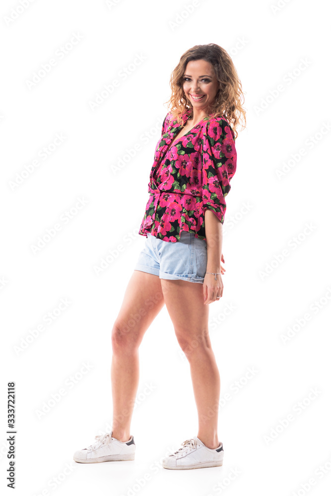 Naklejka premium Relaxed happy young curly hair woman in summer wear smiling and looking at camera with arms down. Side view. Full body isolated on white background. 