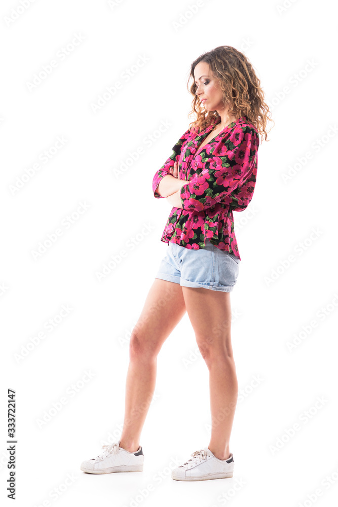 Naklejka premium Sad disappointed young curly hair woman in summer clothes standing with crossed arms looking down. Side view. Full body isolated on white background. 