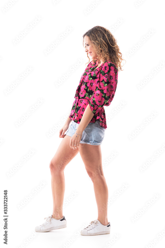 Side view of smiling shy beautiful girl with curly hair in trendy casual summer fashion. Full body isolated on white background. Side view of smiling shy beautiful girl with curly hair in trendy casual summer fashion. Full body isolated on white background.