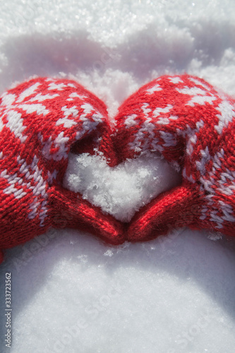 Hands in the mittens form a heart from the snow