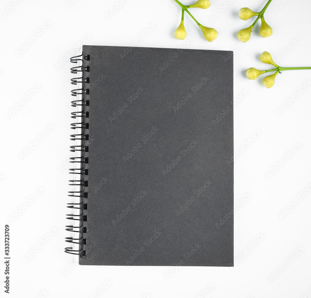 Gray colored paper diary and some small flowers before a white background